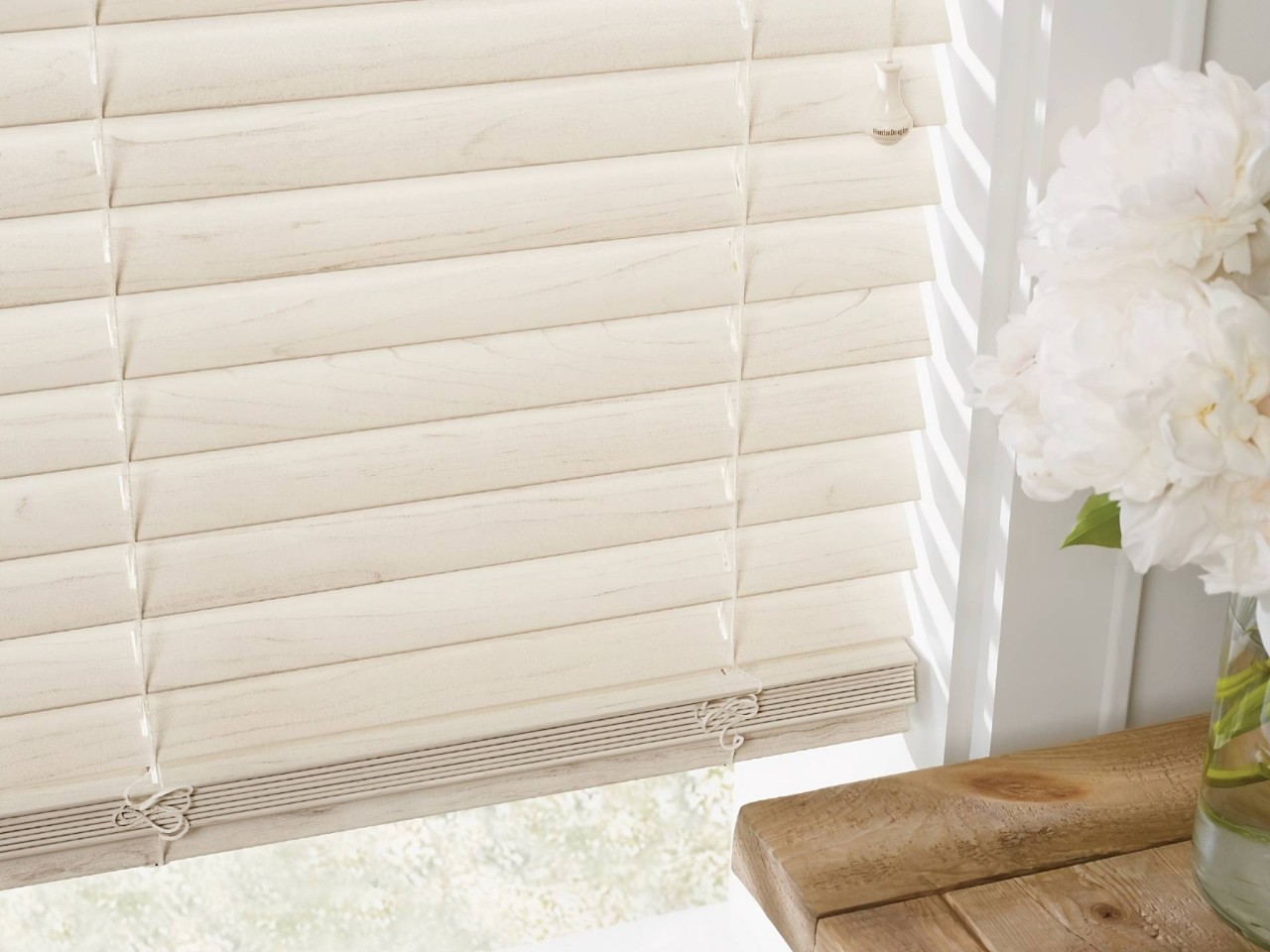 Close-up of cream-colored Hunter Douglas EverWood® Faux Wood Blinds with white flowers to the right-hand side at Wessco Blinds near Seattle, WA